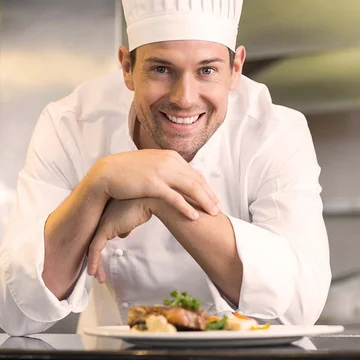 Glücklicher Koch von apetito cateing grinst und freut sich seine Gäste mit leckeren Speisen frisch aus der Küche zu begeistern