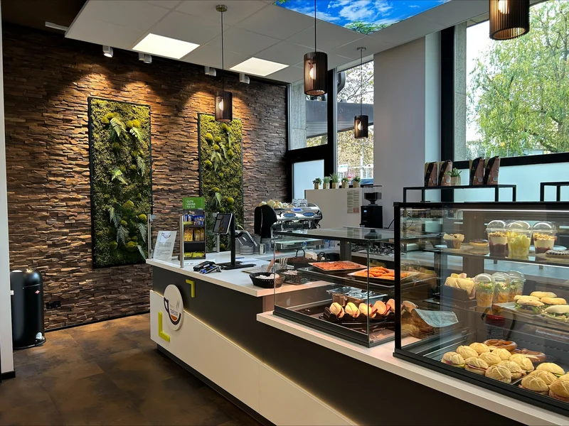 Eine schwarz, weißen Auslage gefüllt mit verschiedener Backwaren und Obst. Neben einer steinigen braunen Wand mit Moos Elementen. 